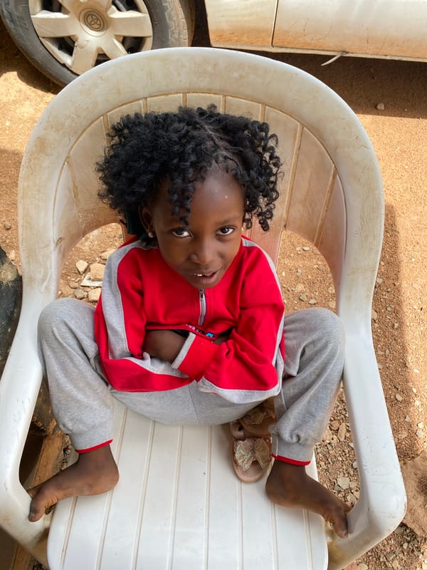 Girl in tracksuit sits outdoors in plastic chair, Nigeria