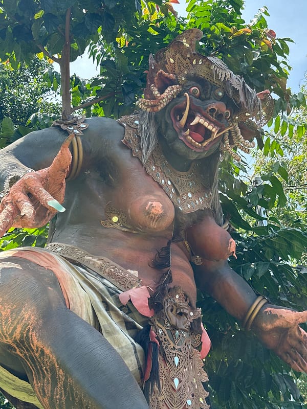Tourist documents Balinese waterfall site with demon statues, bottle art