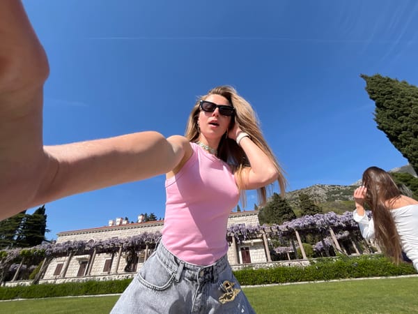 Woman photographs blooming wisteria pergola in Sveti Stefan