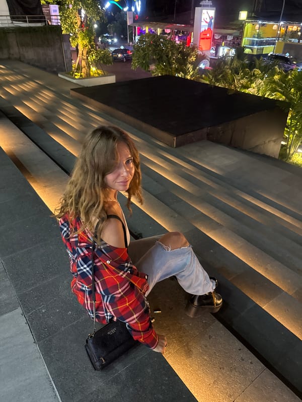 Woman in plaid shirt sits on lit stone steps in Kuta