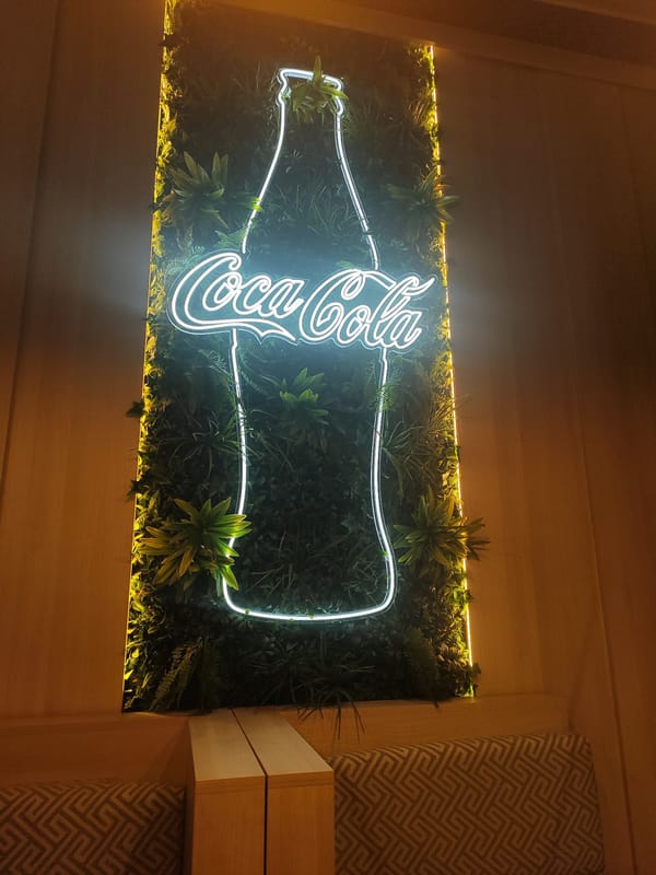 Neon Coca-Cola bottle sign mounted on green wall display