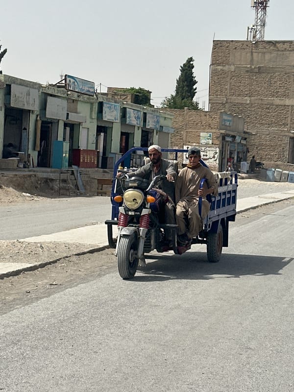 Two men ride motorcycle with trailer through Quetta streets