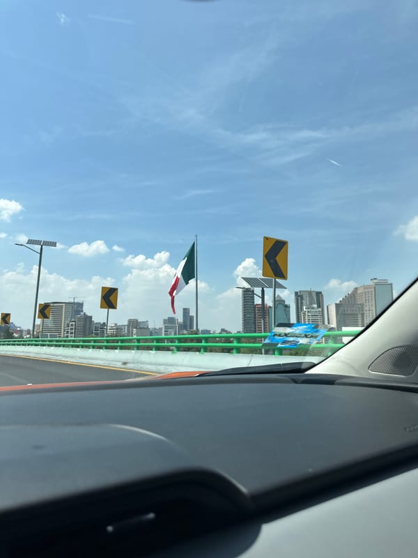 Vehicle travels Mexico City highway past flag bridge, Ferris wheel