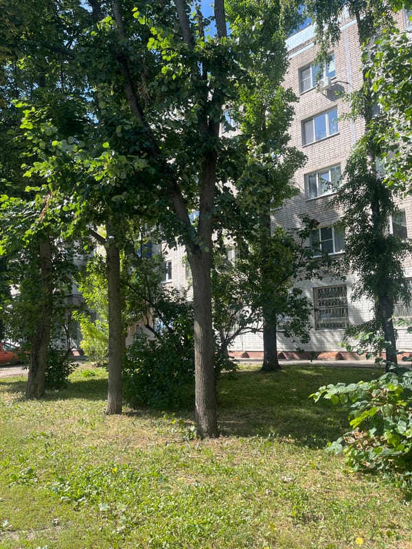 Light-brick apartment building tucked behind summer greenery in Voronezh