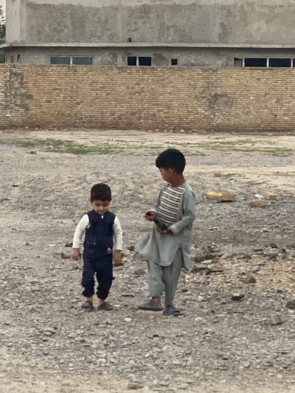 Two young men stand on unpaved ground in Kandahar