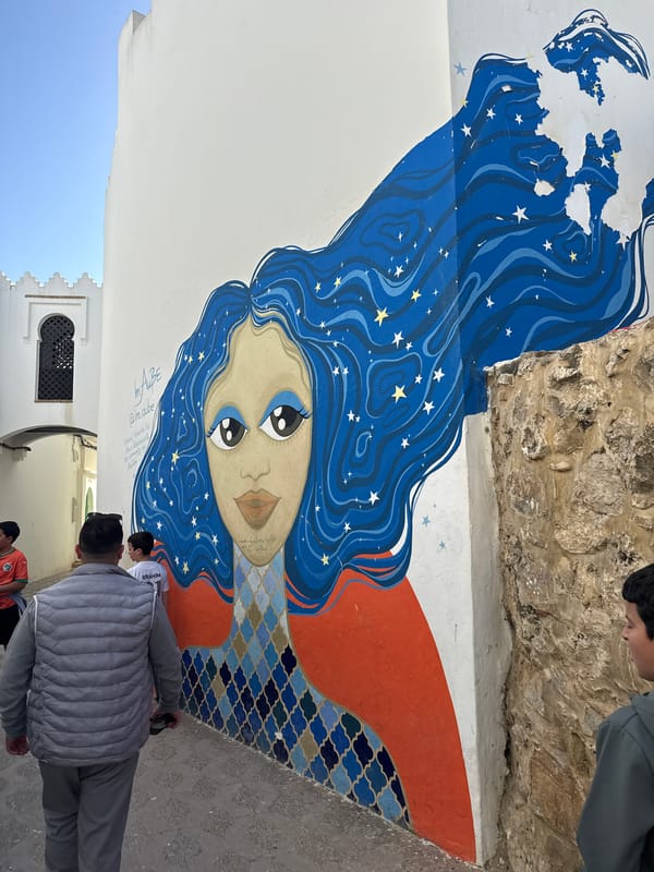 Pedestrians walk narrow streets amid murals in Asilah, Morocco