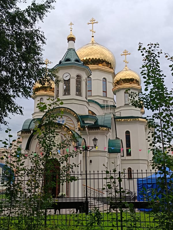 White church with golden domes, clock tower, and colorful flags