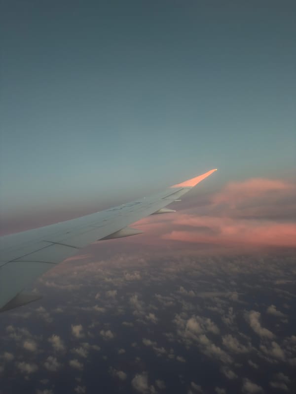 Passenger photographs airplane wing against pink-tinged clouds over Turkey