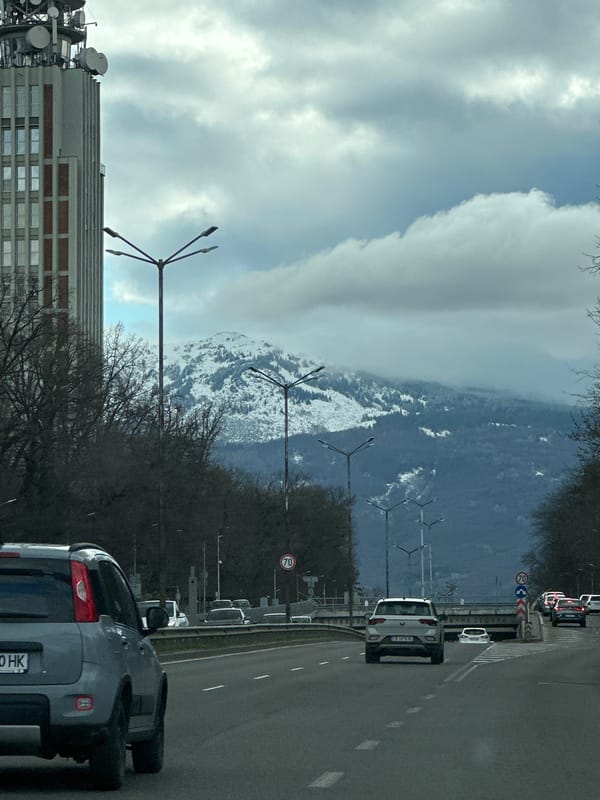 Sofia street view captures snow-capped mountains, antenna building