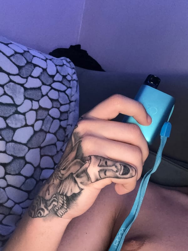Person with tattoos photographed indoors making peace sign gesture