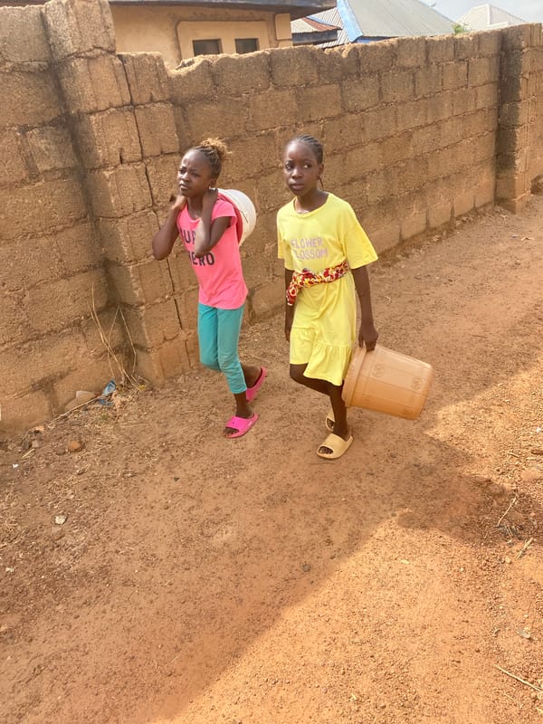 Two girls with bucket observed on dirt path in Bukuru