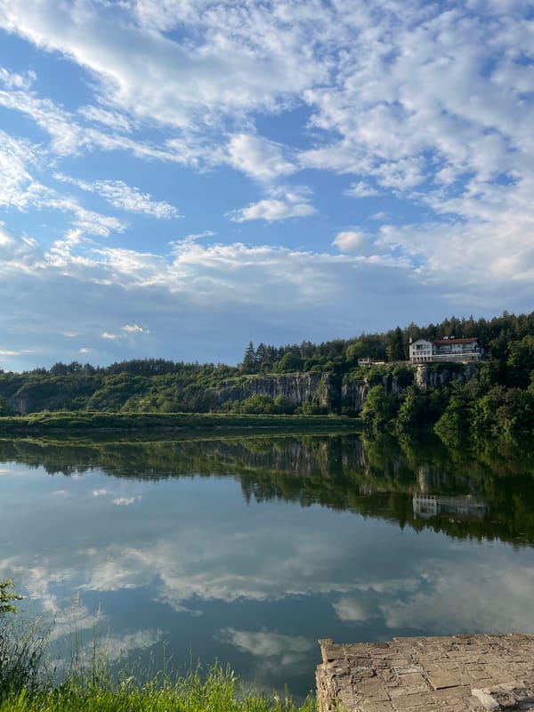 Unidentified waterfront scene with reflective water and rocky cliff documented