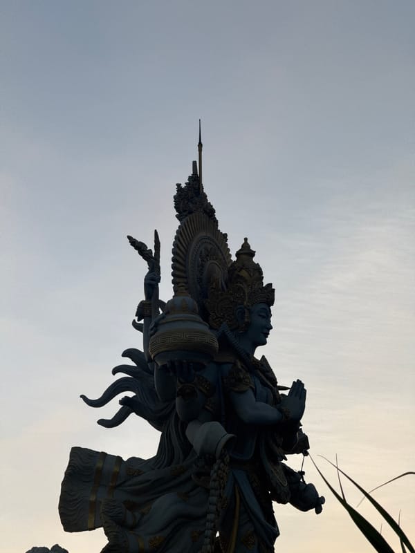 Busy Kuta Beach at sunset — vendors, crowds, and a deity statue