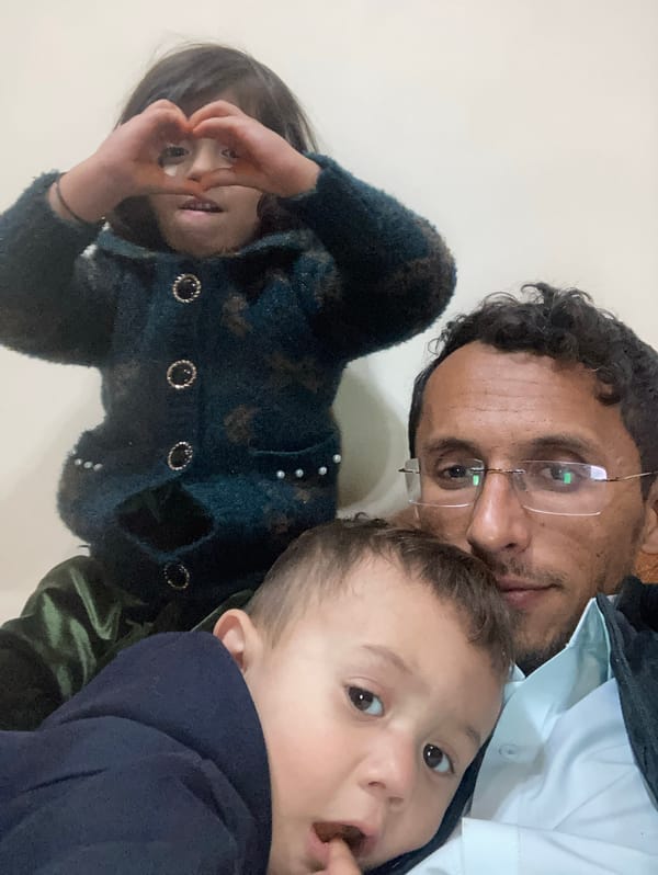 Adult carries child on back while walking Quetta street