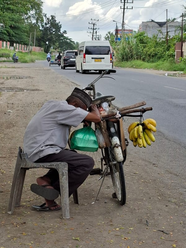 Elderly banana vendor rests roadside with bicycle in Lhokseumawe