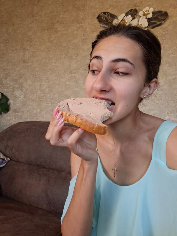 Indoors on a couch, mid-bite into a pâté-topped slice of bread.