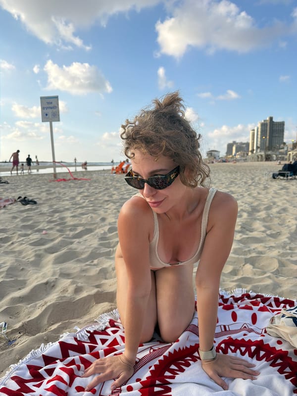 Kneeling pose on a Tel Aviv beach, city skyline behind