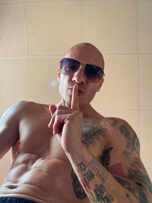 Tattooed, shirtless figure poses in tiled Pleven interior