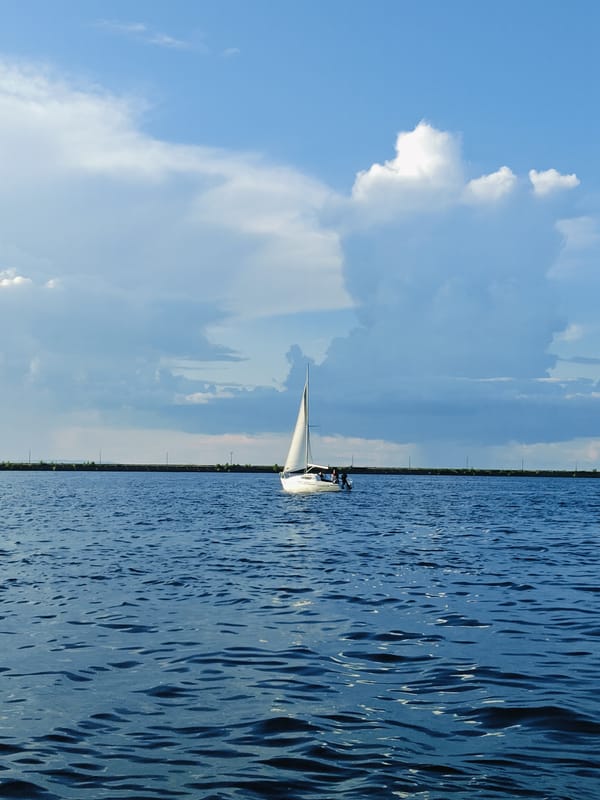 Sailboat and barge share calm water near Chaikovsky riverfront