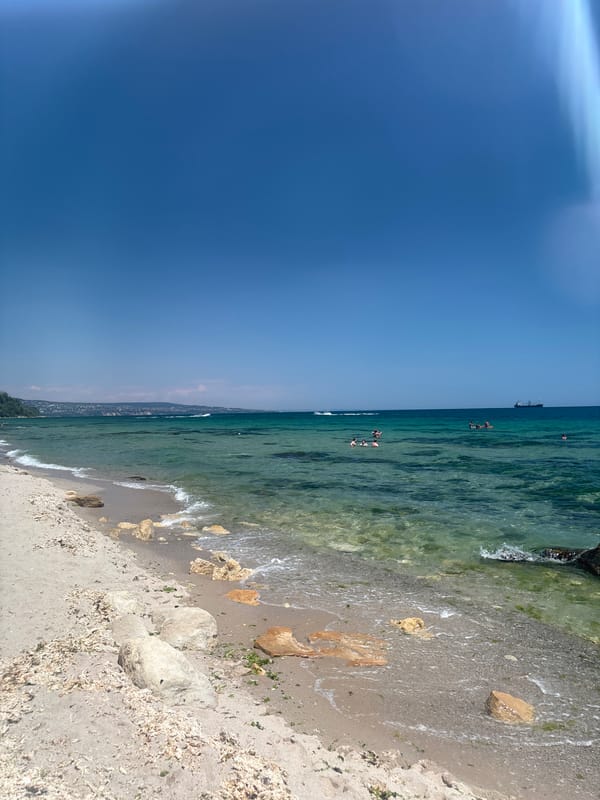 Calm turquoise shoreline with rocky sand under clear skies