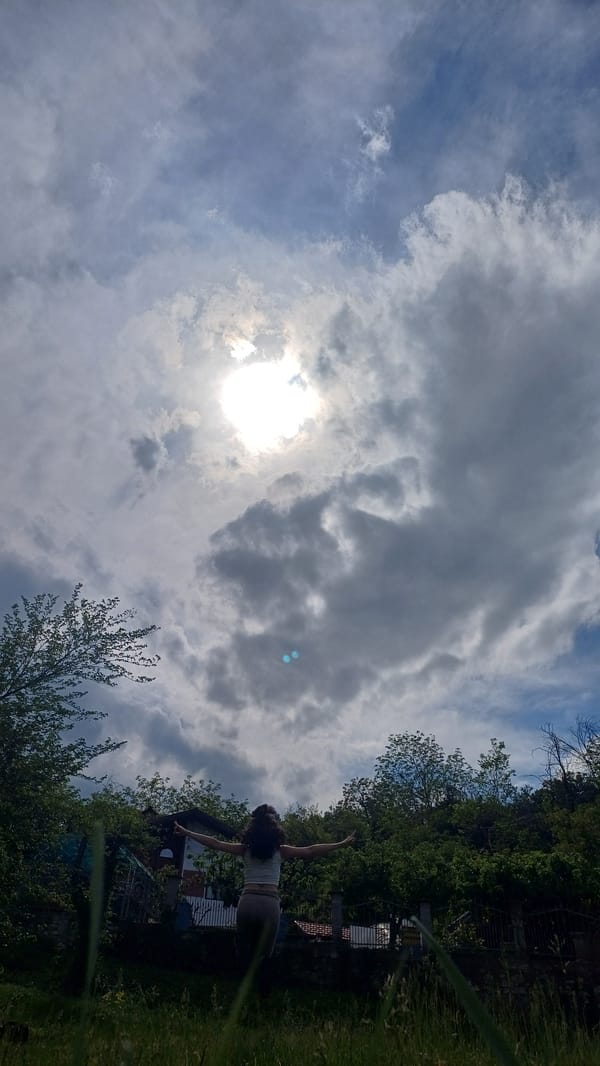 Person stands arms outstretched in Bulgarian field under cloudy skies