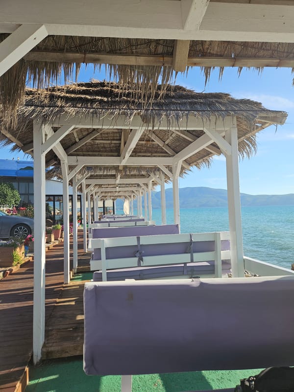 Thatched sun shelters documented along waterfront deck in Orikum