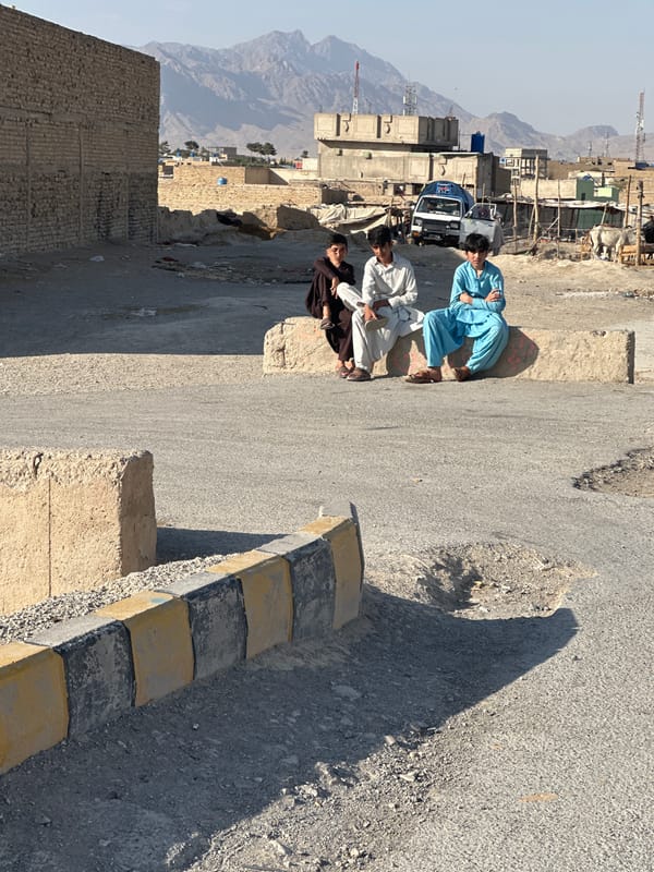 Three people on concrete barrier in dusty Quetta streets