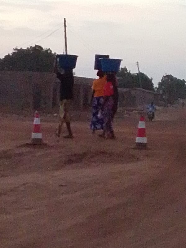 Three people carry blue containers on dirt road