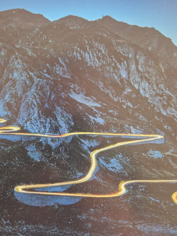 Light trails curve through a dramatic mountain road at night