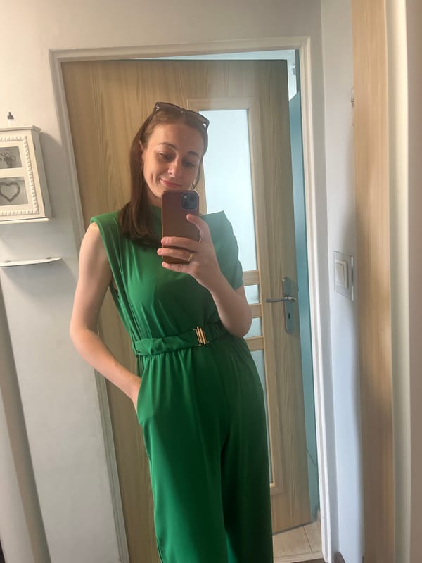 Woman documents green jumpsuit outfit in extended hallway mirror selfie session