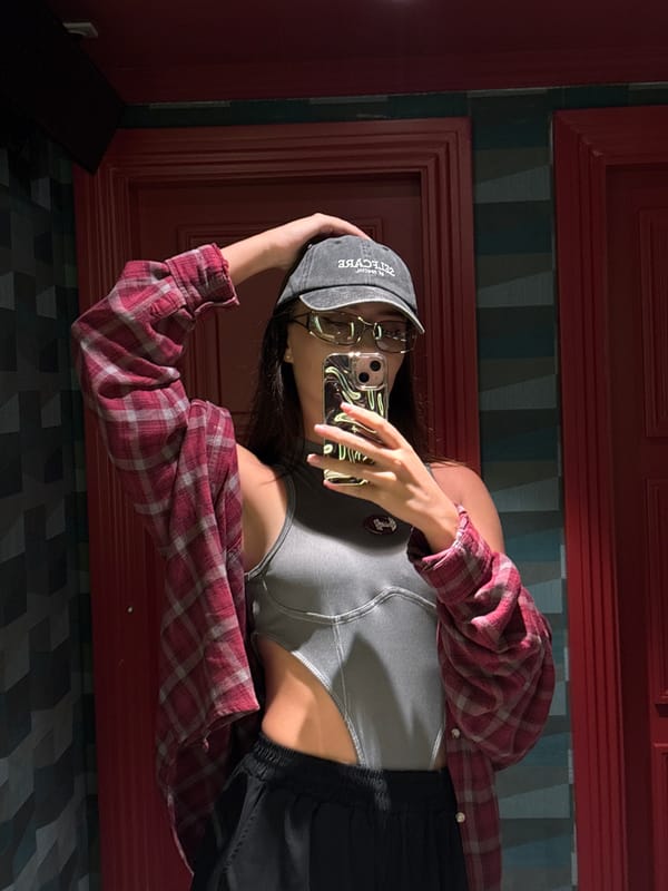 Mirror selfie in a dim room, layered plaid and cutout top