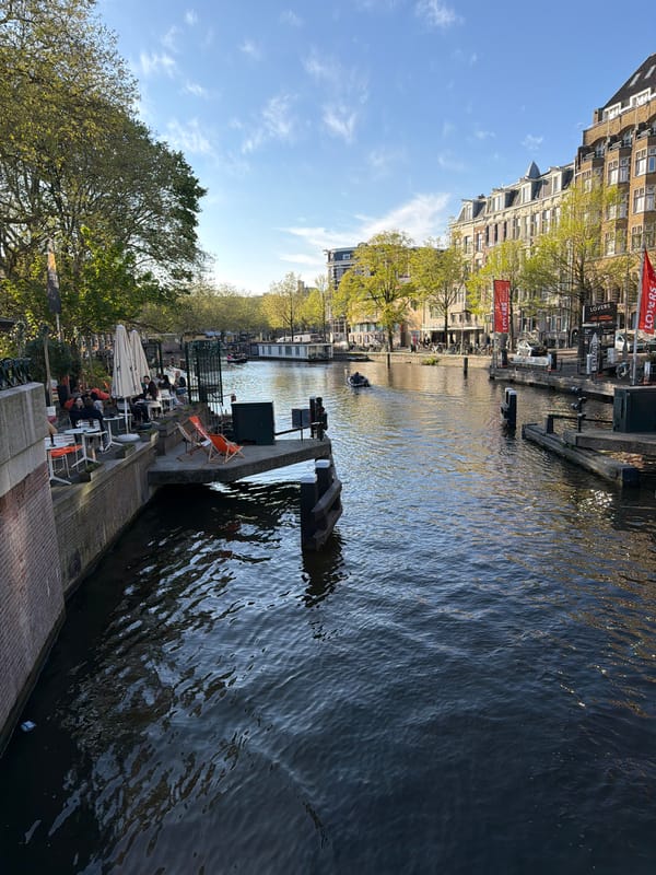 Red tour boat cruises Amsterdam canals on sunny afternoon