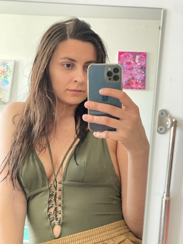 Woman takes bathroom mirror selfies in olive tank top