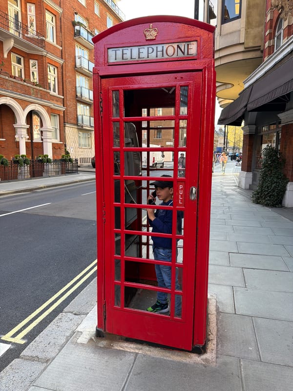 Child poses in red phone booth as family crosses London street