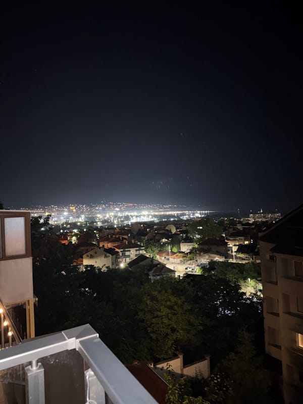 Nighttime cityscape views captured from balcony with cocktail bottle