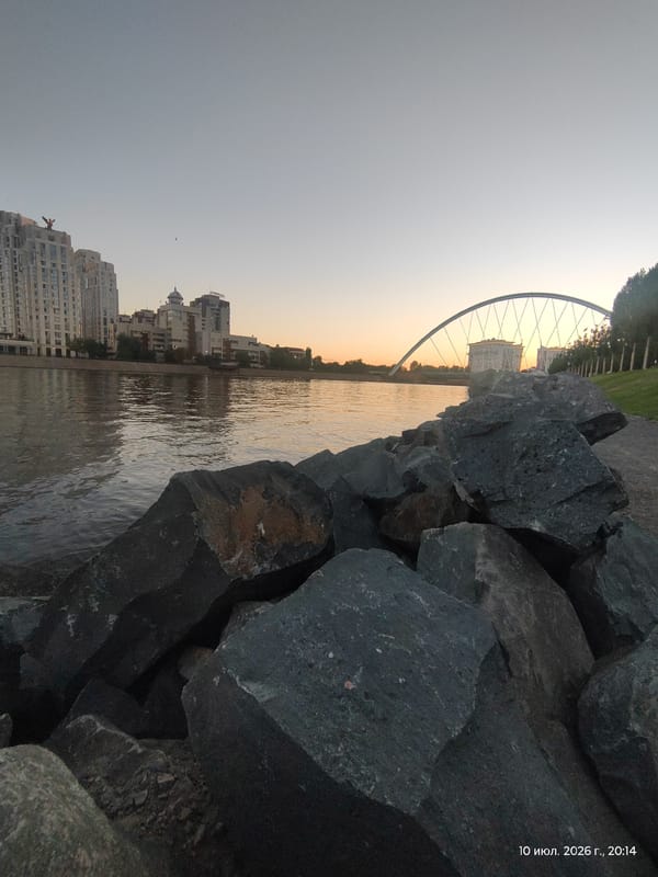 Astana riverfront at golden hour: water, skyline, and statue