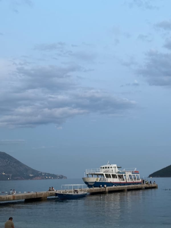 Budva waterfront at dusk: ferry docked, kayaks on the beach