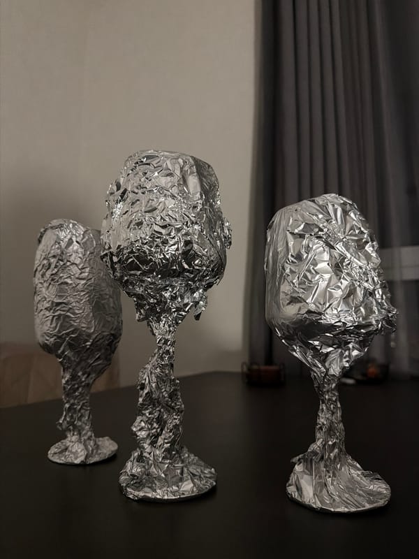Person wraps wine glasses in foil, cat investigates