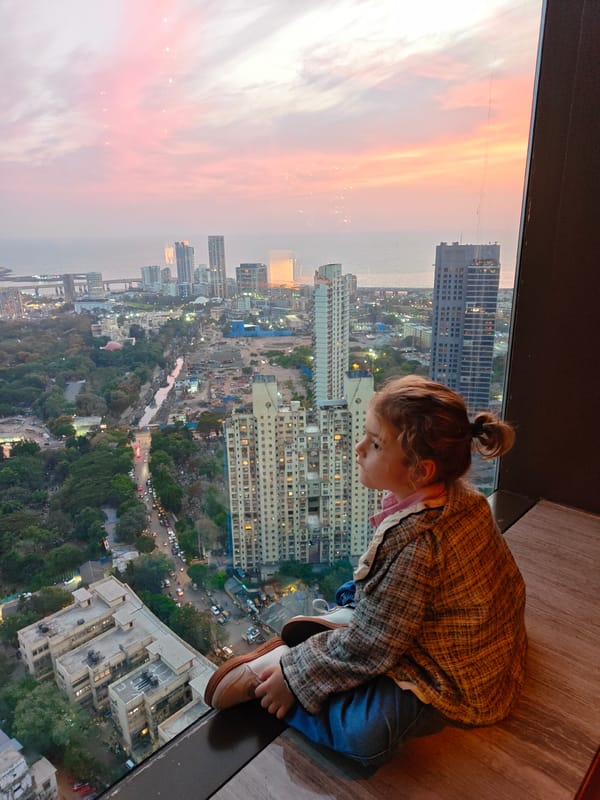 Child watches Mumbai sunset from window ledge during cityscape viewing