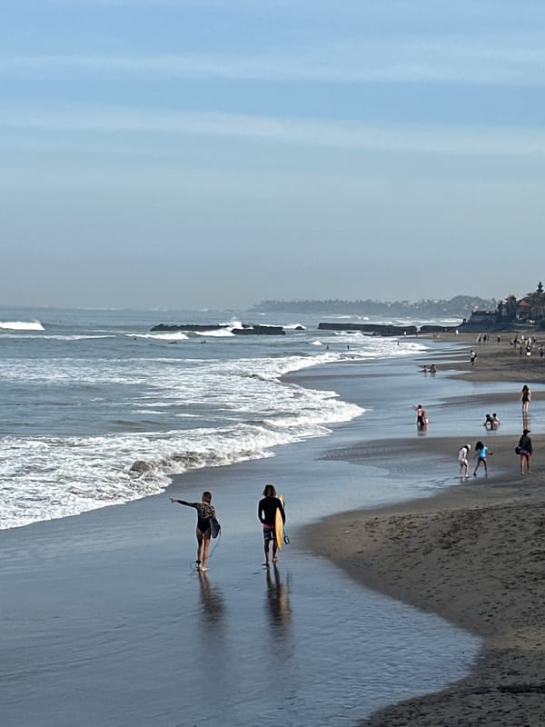 Surfers and beachgoers on North Kuta's dark sand shore