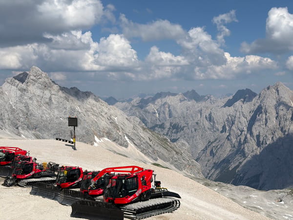 Red snow groomers parked against Garmisch's rocky alpine peaks