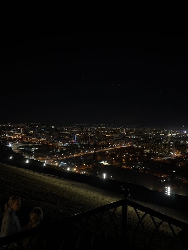 Nighttime gathering at illuminated Krasnoyarsk chapel with fireworks, city views