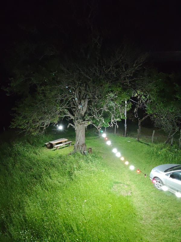 Lit outdoor space at night with parked car and picnic area
