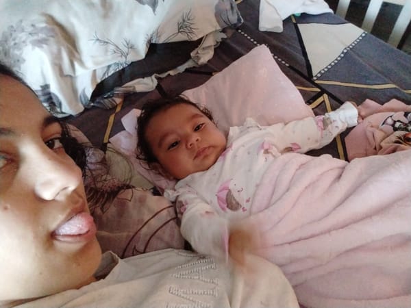 Woman takes playful selfie with baby on pink bedding