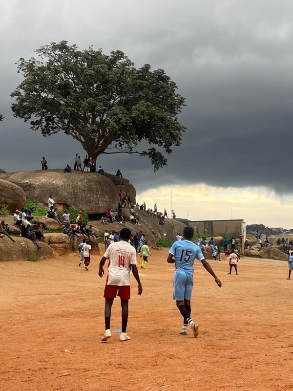 Football match on a dusty Jos pitch under gathering storm clouds