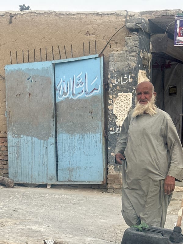 Elderly man stands by weathered blue door in Quetta