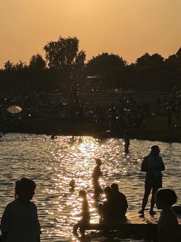 Crowded lakeside beach scene at sunset, swimming and wading