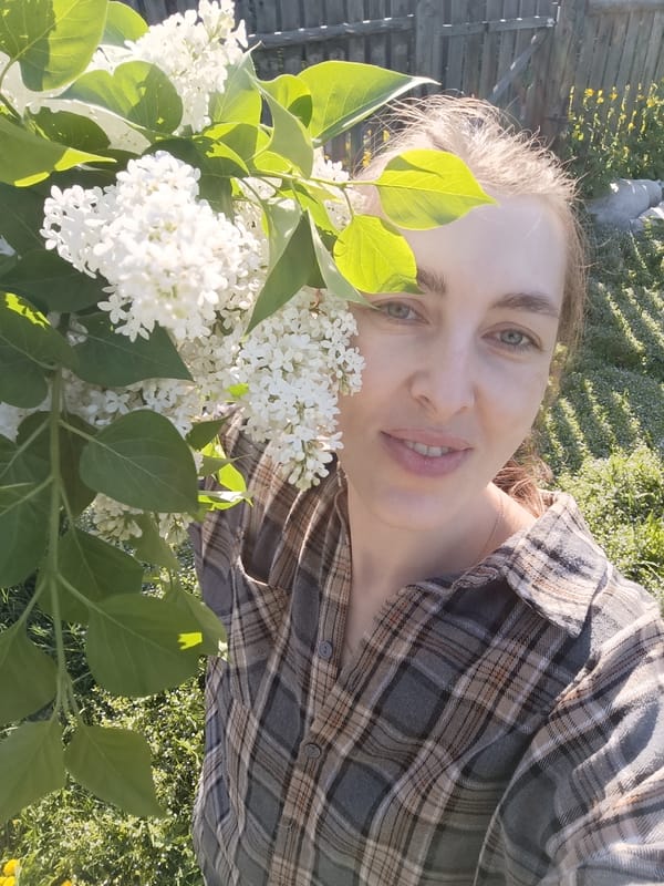 Woman poses near white lilac blossoms in outdoor setting