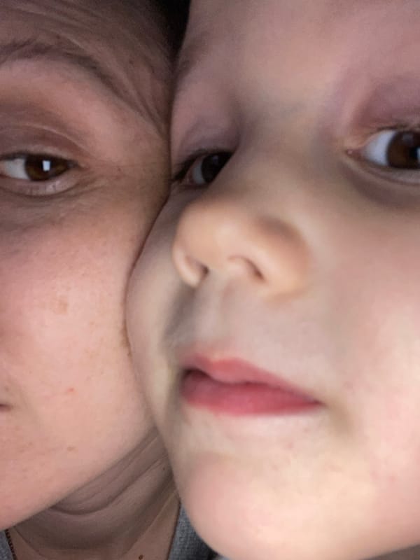 Child with heart plush toy photographed near coniferous tree