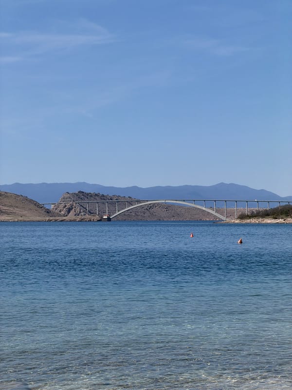 Clear day captures Krk Bridge and beachgoer in Jadranovo